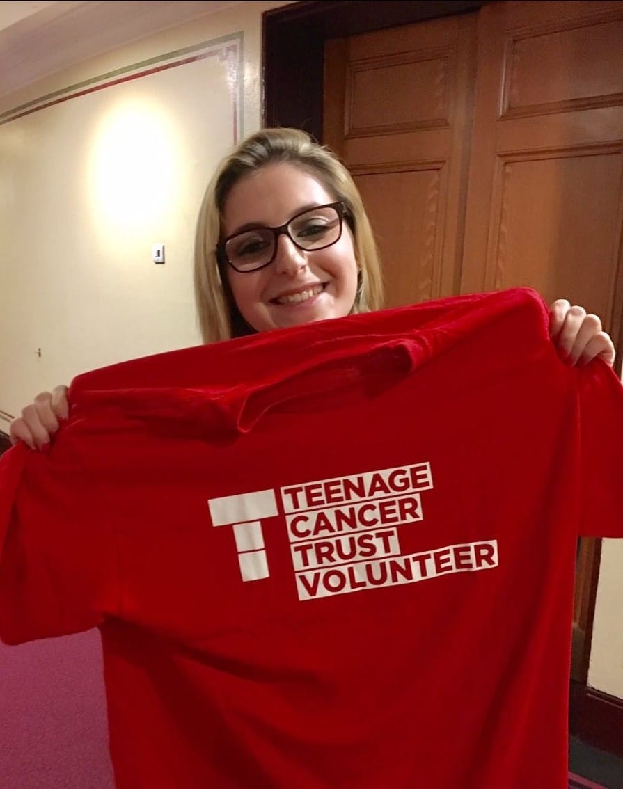 Chloe Woolfe holding up Teenage Cancer Trust logo t shirt