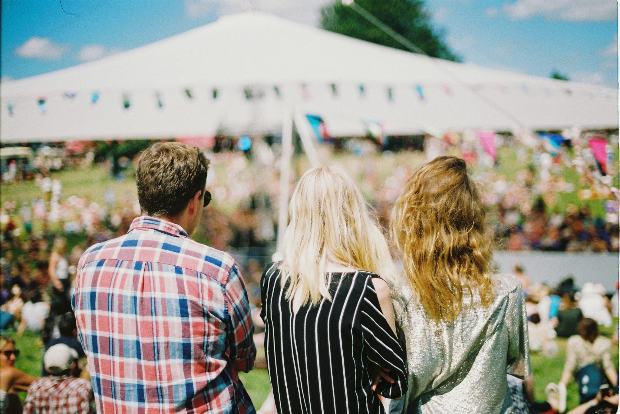 View of outdoor arena from behind three people amongst crowds at festival